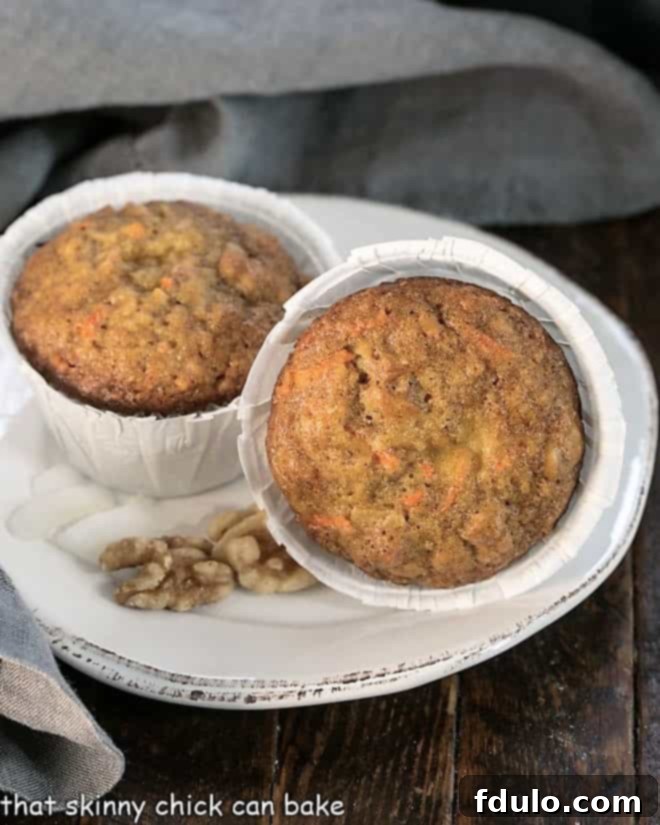 Two Cream Cheese Filled Carrot Cake Muffins on a round white plate, showing the beautifully baked tops.