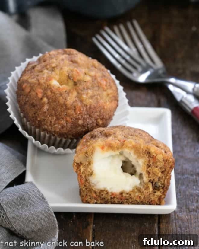 A carrot cake muffin cut in half to reveal the gooey cream cheese center on a square white plate, demonstrating the hidden surprise.