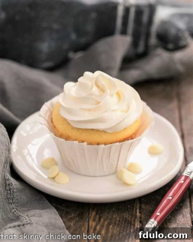Ghirardelli Vanilyalı Cupcakeler, Beyaz Çikolatalı Swiss Meringue Kreması ile yuvarlak beyaz bir tabakta, yanında beyaz çikolata parçacıkları.