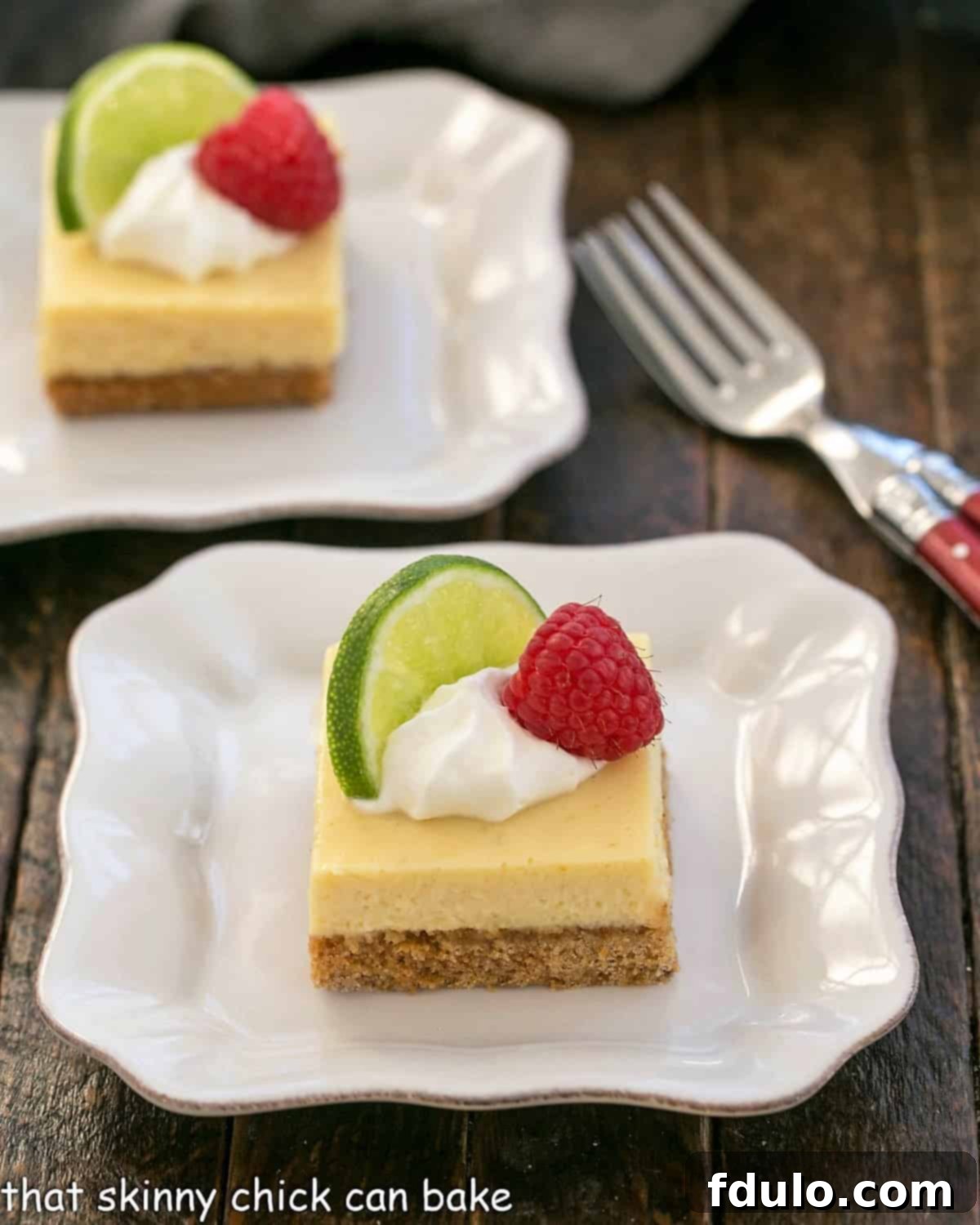 Two perfectly arranged Key Lime Pie Bars, each on a small white plate, accompanied by elegant red-handled forks. The vibrant green filling and golden-brown crust are clearly visible, inviting a taste.