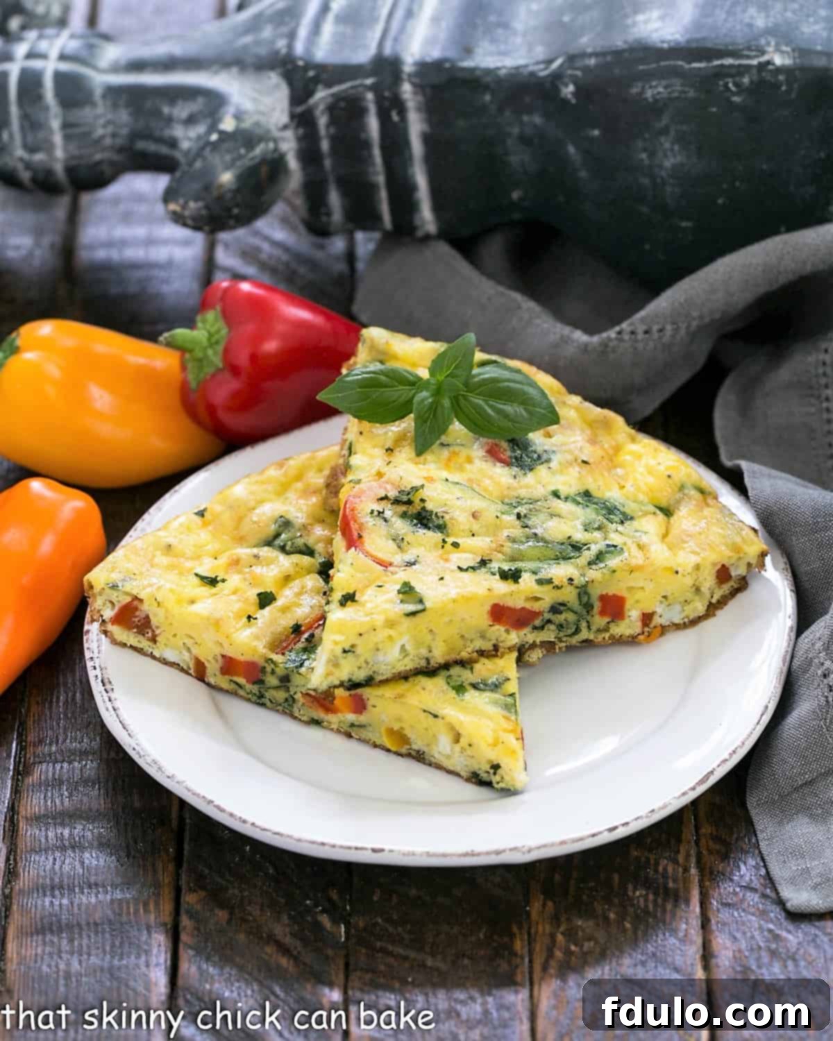 2 slices of egg frittata on a white plate with mini peppers in the background. A delicious, healthy Spinach Bell Pepper Frittata ready to serve.