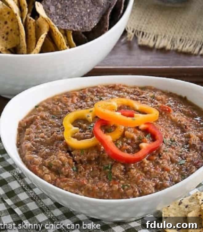 Smoky Black Bean Dip in a pristine white serving bowl, garnished with a sprig of fresh cilantro, against a rustic backdrop, highlighting its vibrant texture and inviting presentation.