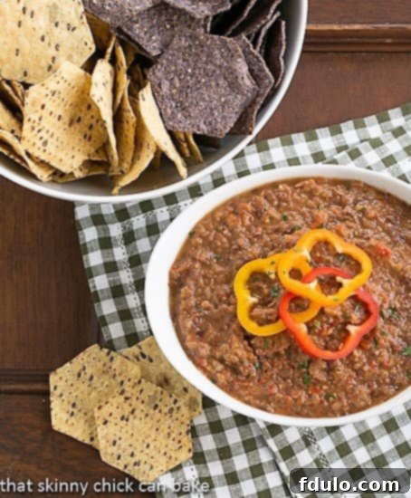 Smoky Black Bean Dip in a white bowl with a bowl of crispy tortilla chips on a wooden surface, ready for a delicious snack or party appetizer.