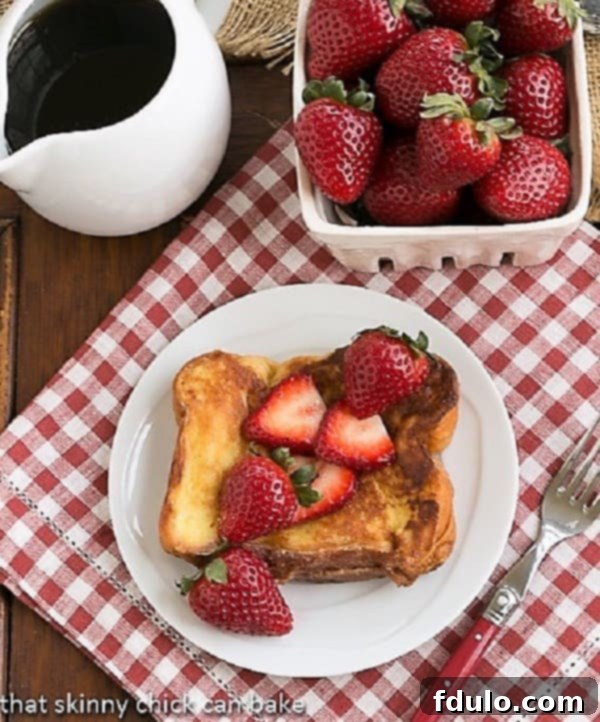 Overhead view of Strawberry Mascarpone Stuffed French Toast served with a generous pour of maple syrup and a small basket of fresh strawberries, highlighting its gourmet appeal.