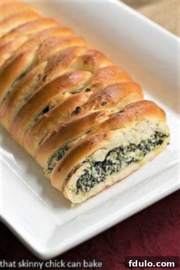 Spinach and Onion Braid on a long white platter with the filling exposed, showing layers of cheesy spinach and golden crust.