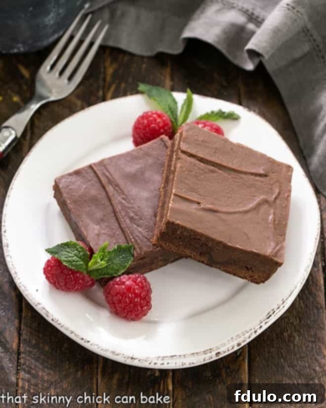 Decadent Infused Chocolate Brownies 2 An overhead view of two exquisitely prepared chocolate poke cake brownies, artfully arranged on a pristine round white dessert plate, ready to be enjoyed.