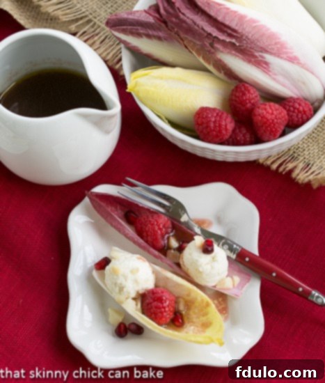 Close-up of Endive Cups with Blue Cheese, Raspberries and Macadamia Nuts on a square white plate with a delicate drizzle of raspberry vinaigrette.