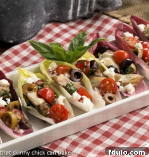 Mediterranean Endive Boats - a fun, bite-sized salad or appetizer A pristine white ceramic tray elegantly presenting a collection of endive leaves, each meticulously filled with a vibrant salad mixture.