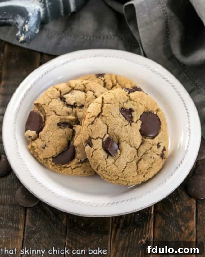 Easy Chocolate Chip Cookies - Big, chewy chocolate chip cookies with caramel undertones! Overhead view of several jumbo chocolate chip cookies arranged invitingly on a white plate, showcasing their generous size and melted chocolate.