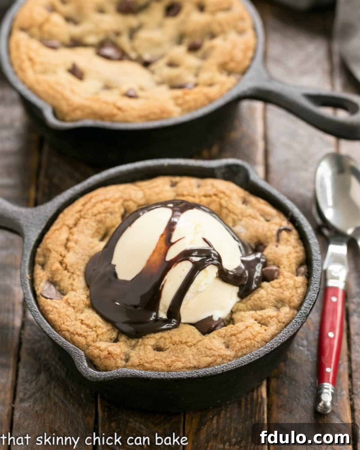 Two large, golden-brown pizza cookies in cast iron skillets, one topped with melting vanilla ice cream and chocolate syrup, ready to be served.