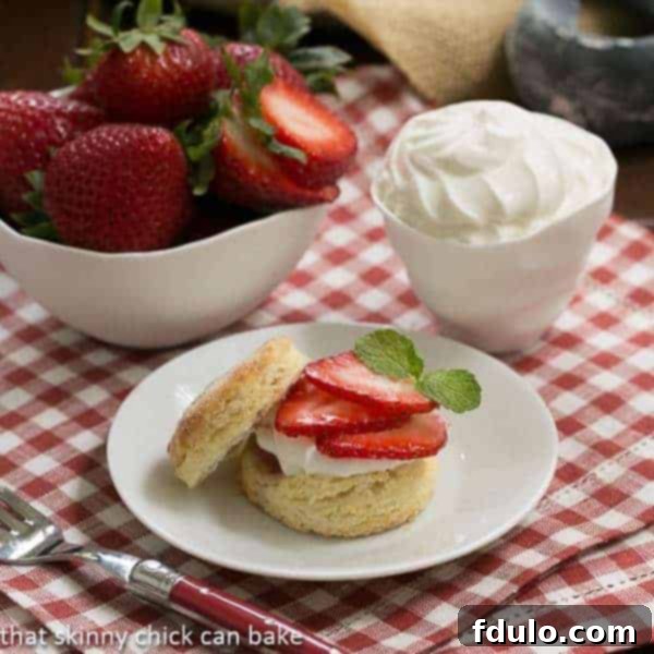 Double strawberry rose shortcake on a white plate next to bowls of strawberries and cream