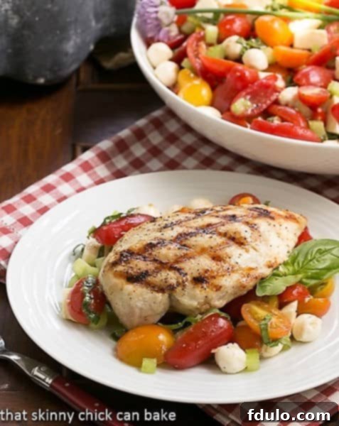 Grilled chicken breast over a vibrant Caprese Salad with Chicken, featuring fresh mozzarella, juicy tomatoes, and green basil.