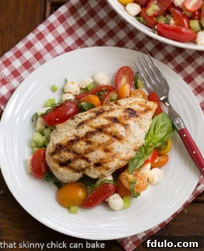Overhead view of grilled chicken breast artfully arranged over a fresh Caprese salad, ready to be served.
