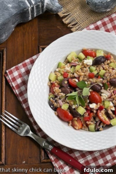 Overhead view of Greek Farro Salad in a white bowl on a red and white checked napkin.