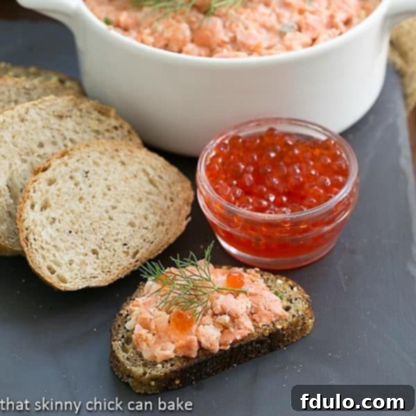 Salmon Rillettes served elegantly in a terrine, accompanied by a small jar of vibrant salmon caviar for garnish, on a white background.