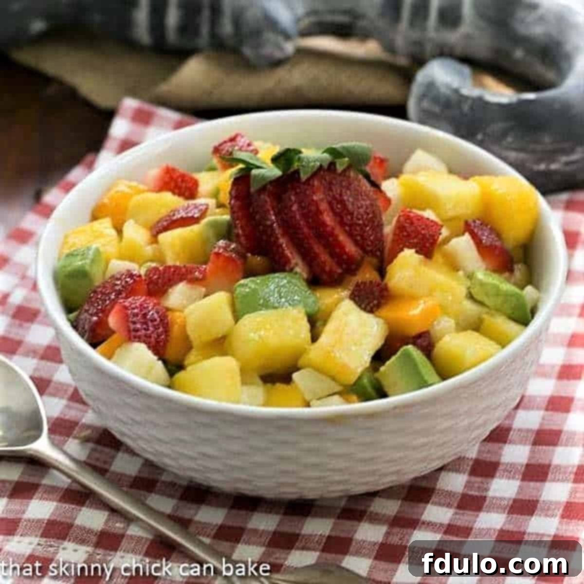 Mango Strawberry Avocado Salad in a white bowl with a silver serving spoon.