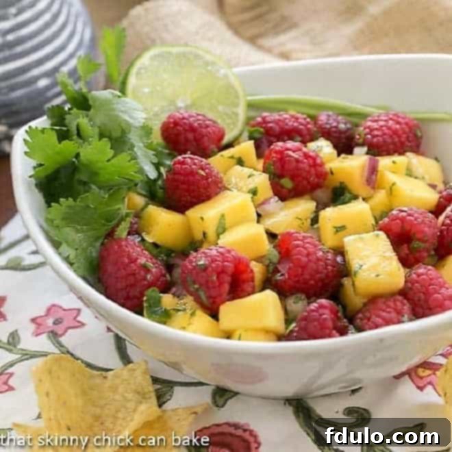 Vibrant Raspberry Mango Salsa in a white bowl, garnished with fresh cilantro and a lime wedge, ready to be enjoyed.