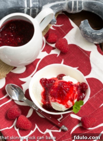 An overhead shot of a delightful Cheesecake Ice Cream Sundae, generously topped with fresh raspberries and a pitcher of homemade raspberry sauce, ready for serving.