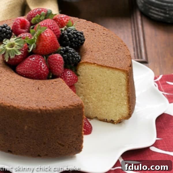 Vanilla Pound Cake - Perfect dessert topped with summer berries or any seasonal topping Whole Vanilla Pound Cake on a white platter with a slice removed and berries piled in the middle.