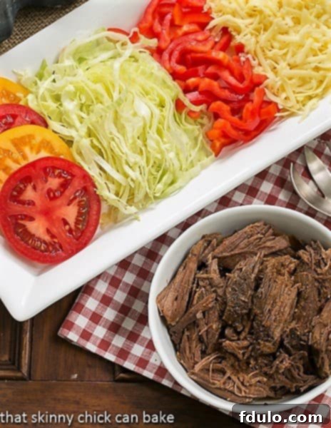 Overhead view of Slow Cooker Beef Barbacoa in a white bowl, richly colored, with a surrounding white tray showcasing various fresh toppings like avocado, cilantro, and radishes.