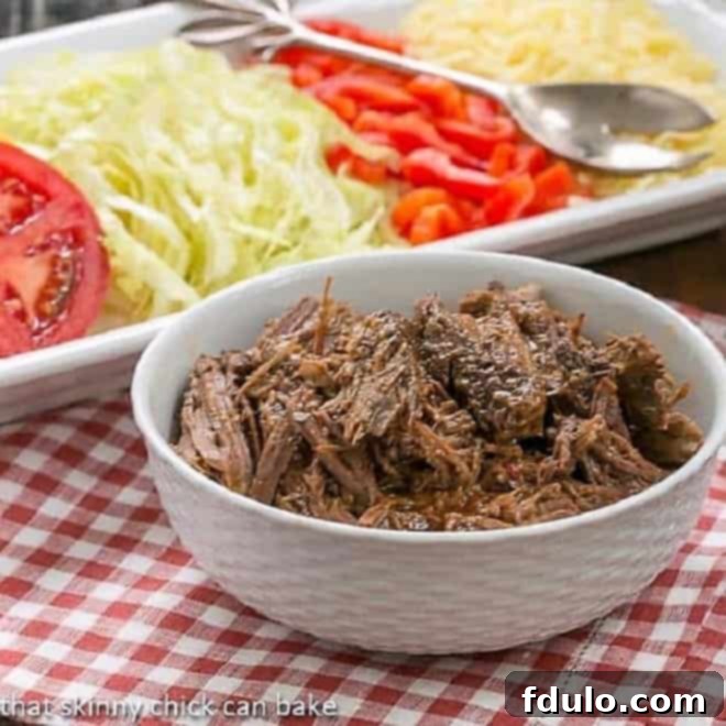 Slow Cooker Beef Barbacoa shredded in front of a white tray of toppings