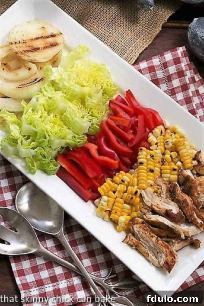 Fresh ingredients for Southwestern Chicken Salad laid out on a white rectangular platter, including chicken, corn, tomatoes, peppers, and cheese.