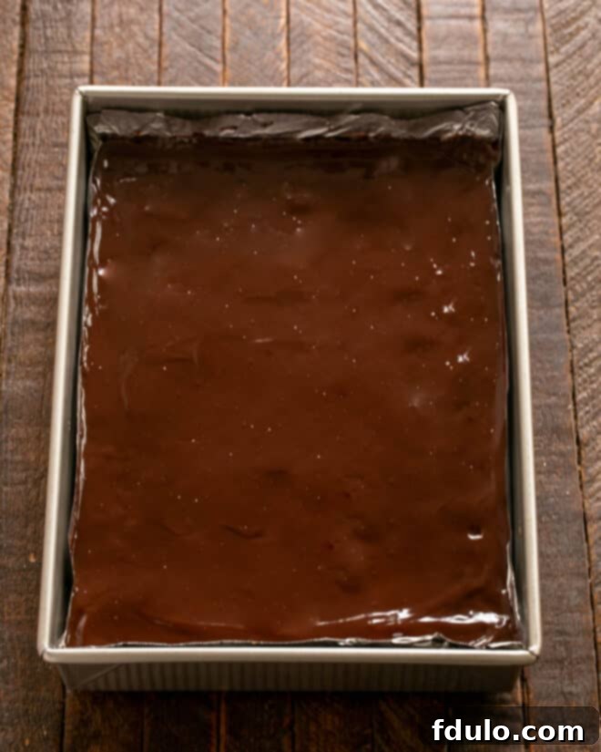 Cooled brownies being topped with ganache.