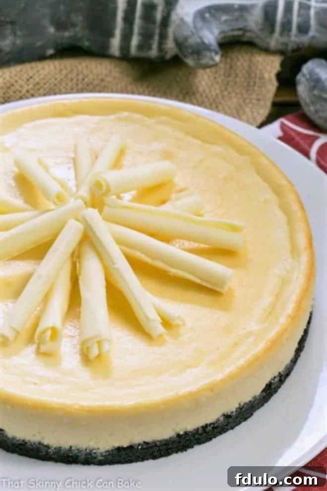 White Chocolate Frangelico Cheesecake - A luscious cheesecake with a chocolate cookie crust, white chocolate and a slosh of Frangelico White Chocolate Frangelico Cheesecake garnished with white chocolate curls on a white cake plate.