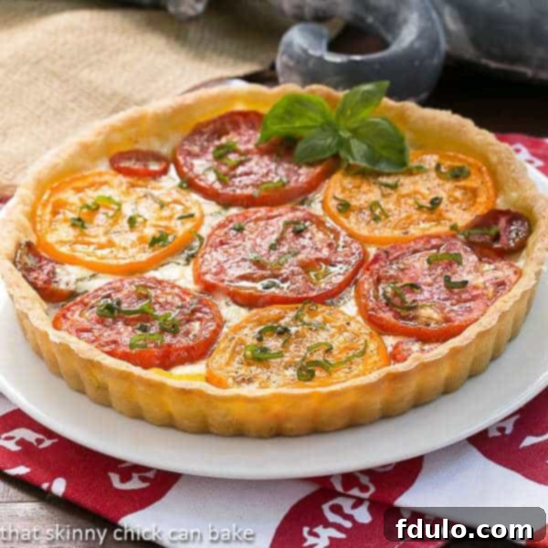 A stunning Summer Tomato Tart on a white serving plate, elegantly garnished with a sprig of fresh basil, ready to be enjoyed.