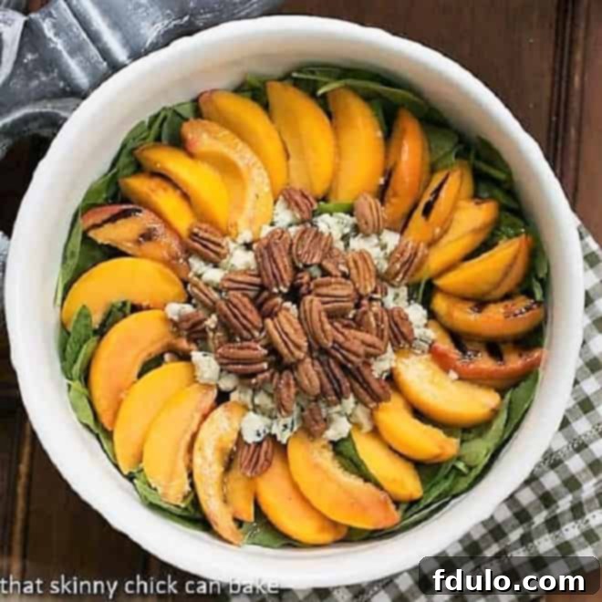 Overhead view of a vibrant bowl of Spinach Salad with Grilled Peaches and Blue Cheese, showcasing fresh ingredients and appealing colors.