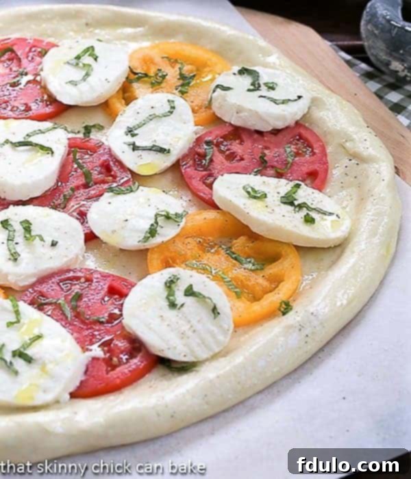 A freshly prepared Pizza Margherita with vibrant red tomatoes, white mozzarella, and green basil leaves, ready for baking.