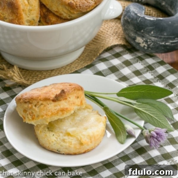 Perfectly baked Herbed Buttermilk Biscuits on a white plate, garnished with fresh sage and chives.