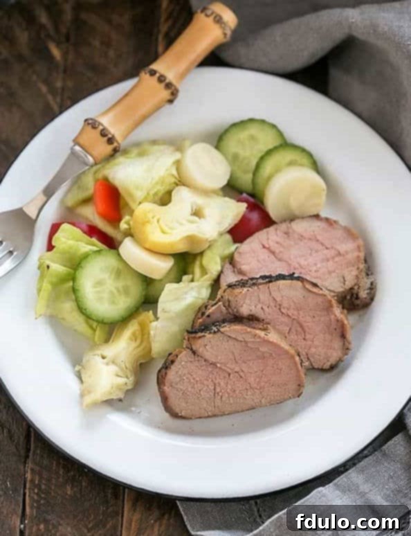 Marinated pork tenderloin sliced on a plate with salad and fork.