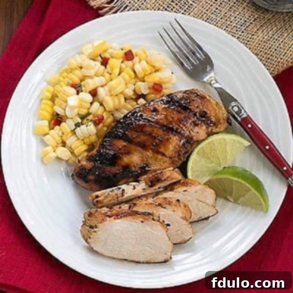 Overhead view of marinated chicken and sides on a white dinner plate with a fork and lime wedges.