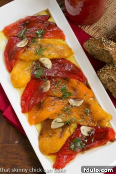Overhead view of glistening Oven Roasted Peppers on a white platter, adorned with sliced garlic and fresh herbs.