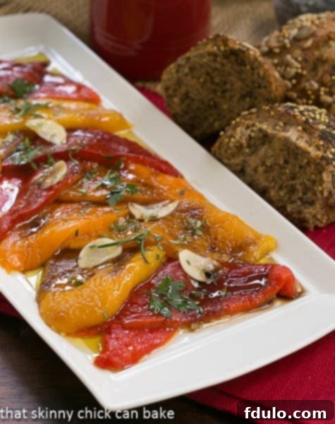 A close-up view of a colorful array of Oven Roasted Peppers, glistening with olive oil and seasoned with herbs, arranged on a white serving tray.