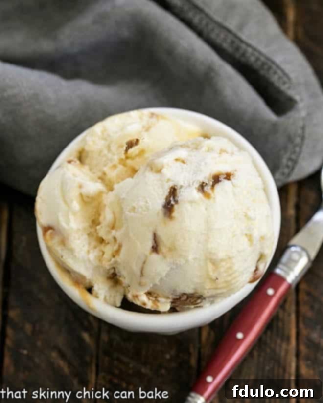 Overhead shot of a pristine white bowl filled with Homemade Vanilla Caramel Swirl Ice Cream, ready to be enjoyed with a cheerful red-handled spoon.
