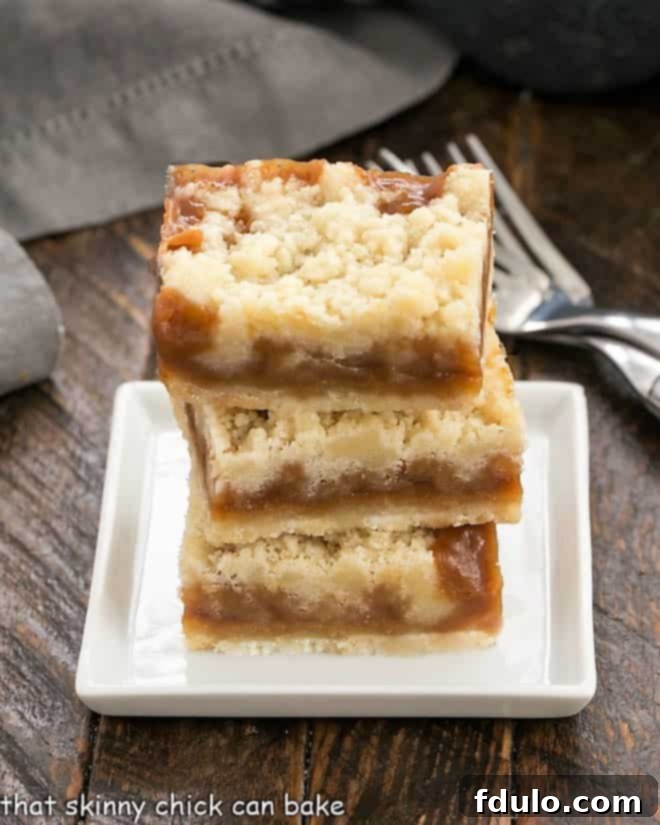Caramel Butter Bars - Simple flavors with delicious results! This Caramel Dessert is easy to make and perfect for caramel lovers!! Three perfectly cut Oatmeal Carmelitas (Caramel Butter Bars) stacked on a small white plate, showcasing the distinct layers of crust, caramel, and streusel.