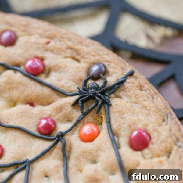 Close-up of a Spiderweb Cookie Cake showing the frosting web and a plastic spider, ready for a Halloween party.
