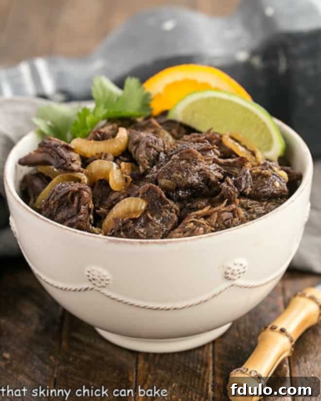 Vaca Frita - Scrumptious Cuban Shredded Beef Vaca Frita in a white bowl over rice and garnished with tomatoes and orange and lime slices.