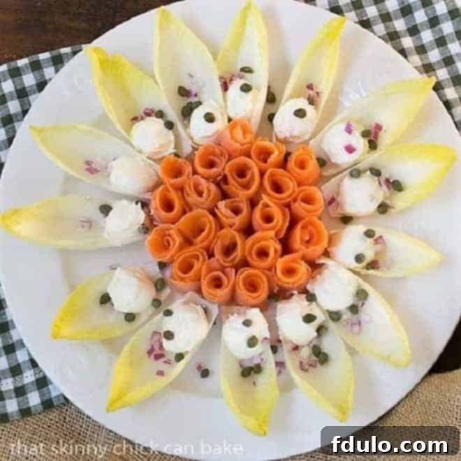 Smoked Salmon Roses with Endive and Creme Fraiche on a round white plate, garnished with dill and capers.