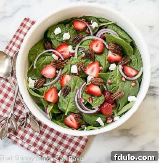 Fresh Spinach, Strawberry, Pomegranate, and Feta Salad in a white serving bowl, placed on a red and white checked napkin.