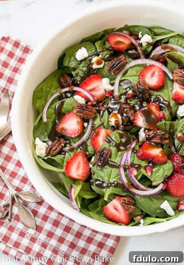 Fresh Spinach, Strawberry, Pomegranate, and Feta Salad, beautifully drizzled with homemade balsamic vinaigrette, in a white ceramic serving bowl.