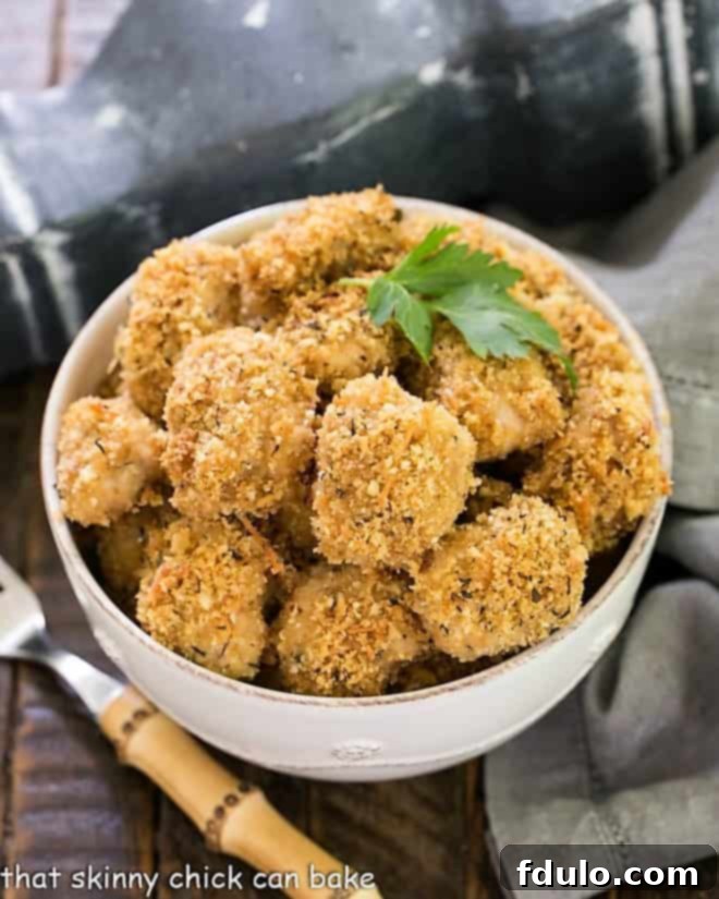 Herbed Chicken Nuggets Recipe - Ditch the drive through and make homemade chicken nuggets for your family! Overhead view of Herbed Chicken Nuggets in a white bowl with a sprig of parsley and a bamboo handle fork, emphasizing their delicious appeal.