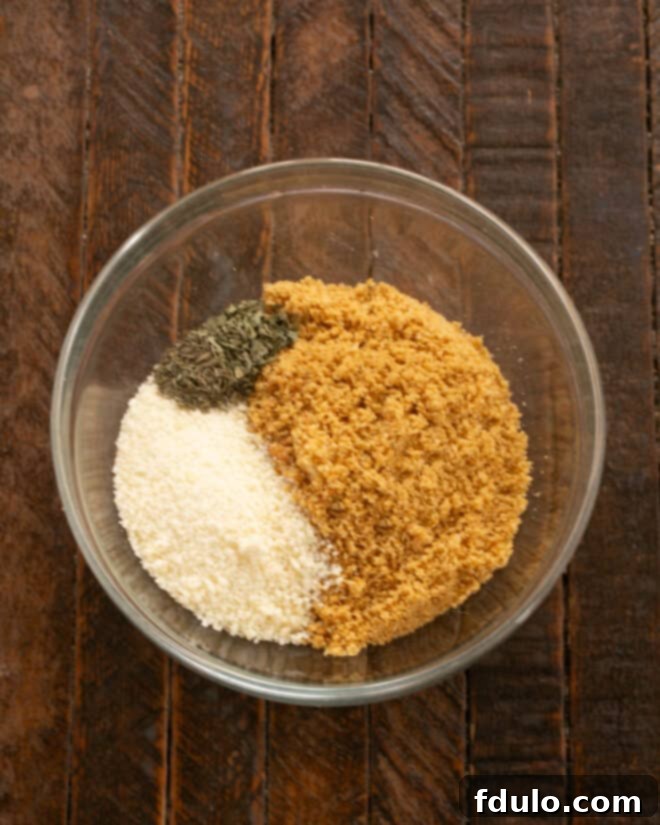 The Ultimate Homemade Chicken Nuggets 3 Step-by-step image of mixing dried basil, thyme, grated Parmesan cheese, and crushed seasoned croutons in a bowl.