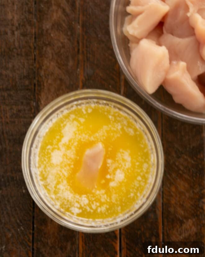 The Ultimate Homemade Chicken Nuggets 4 Step-by-step image of dipping a chicken cube into a bowl of melted butter.