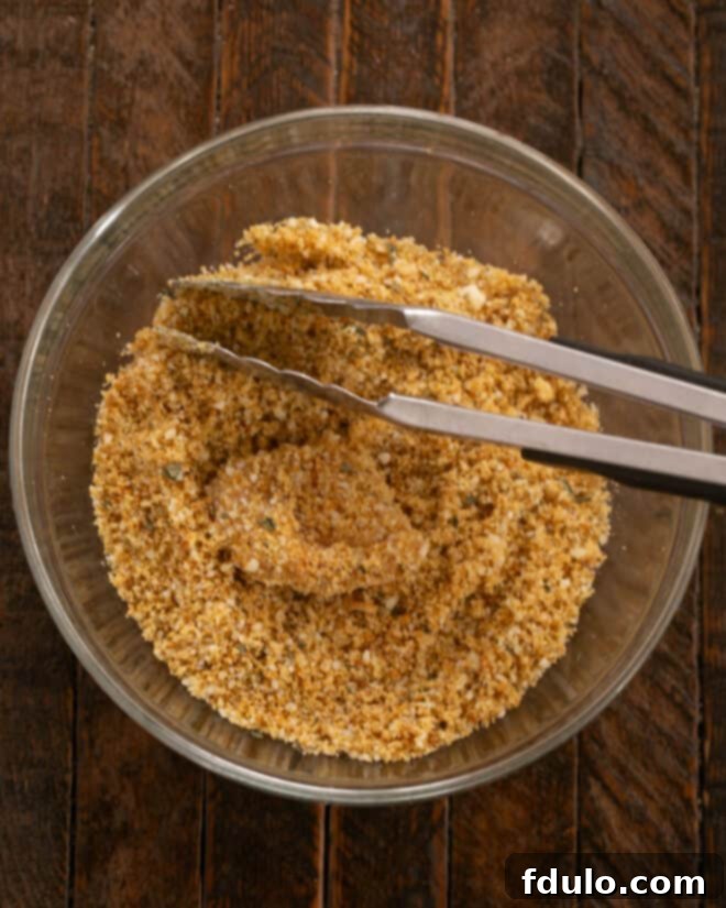 The Ultimate Homemade Chicken Nuggets 5 Step-by-step image of coating butter-dipped chicken cubes in the herb and crouton crumb mixture.