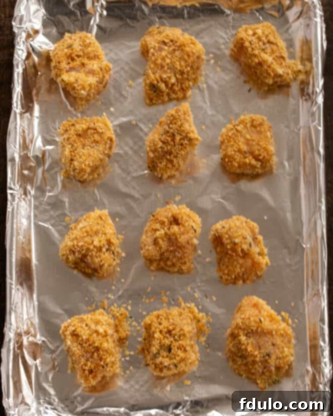 The Ultimate Homemade Chicken Nuggets 6 Step-by-step image of placing coated chicken nuggets on a baking sheet.