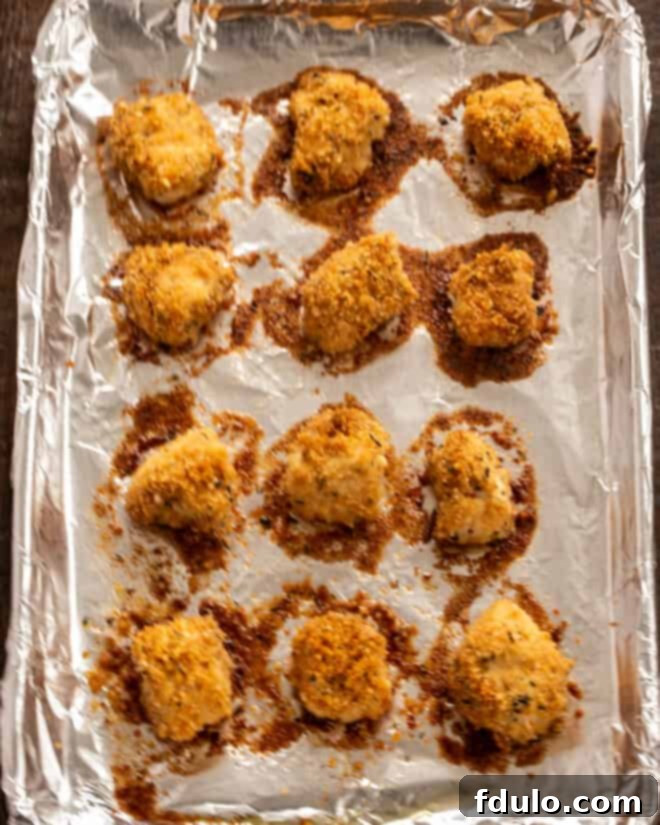 The Ultimate Homemade Chicken Nuggets 7 Step-by-step image of baked herbed chicken nuggets on a baking sheet, golden brown and crispy.