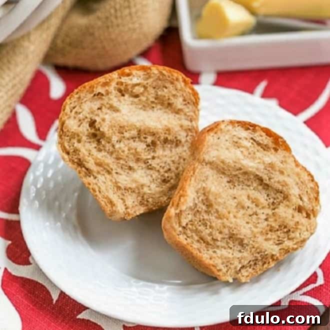 A perfectly baked, golden-brown whole wheat dinner roll on a white plate, gently split open to reveal its soft, airy interior. Steam might still be visibly rising.